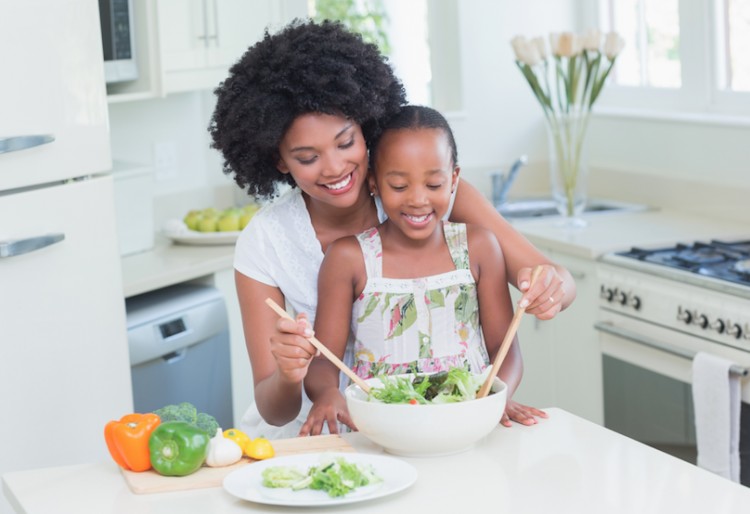 A happy mother and daughter tossing a salad together in the kitchen.