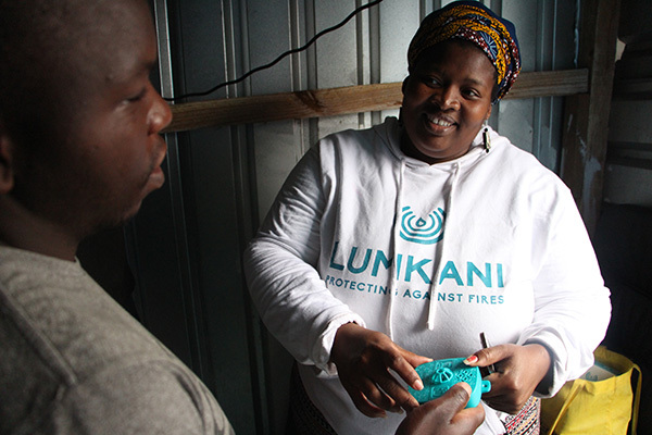 Lumkani worker showing the Lumkani heat detector to an informal settlement resident.