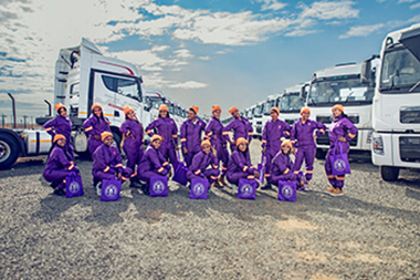 Group of women in transport, posing by the trucks in their Highway Heroes overalls.