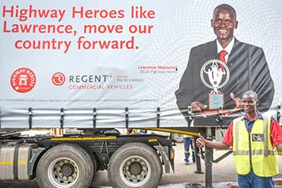Highway Heroes winner Lawrence standing beside a truck trailer with award campaign banner in background