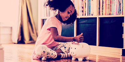 A little girl throwing coins into a piggy bank representing investing in a Hollard Savings Plan