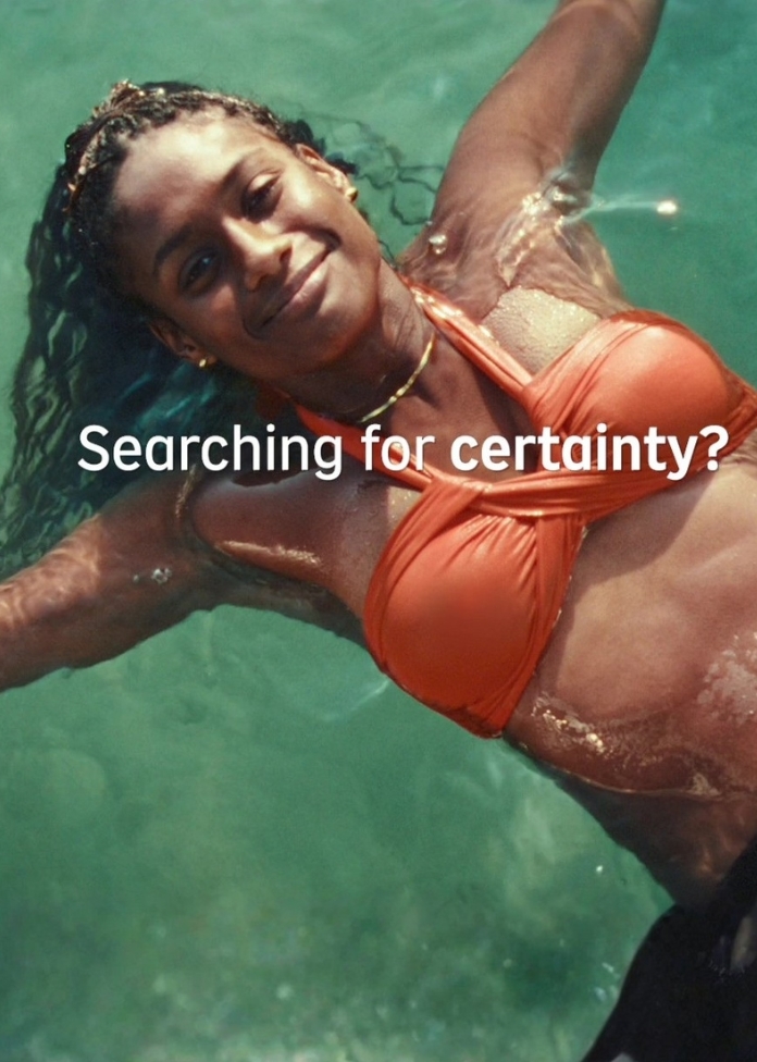 Woman floating in a swimming pool wearing an orange swimsuit, with the text “Searching for certainty?” overlaid on the image.