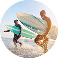 Two Hollard Health Guru clients on the beach, running into the water with their surfboards.