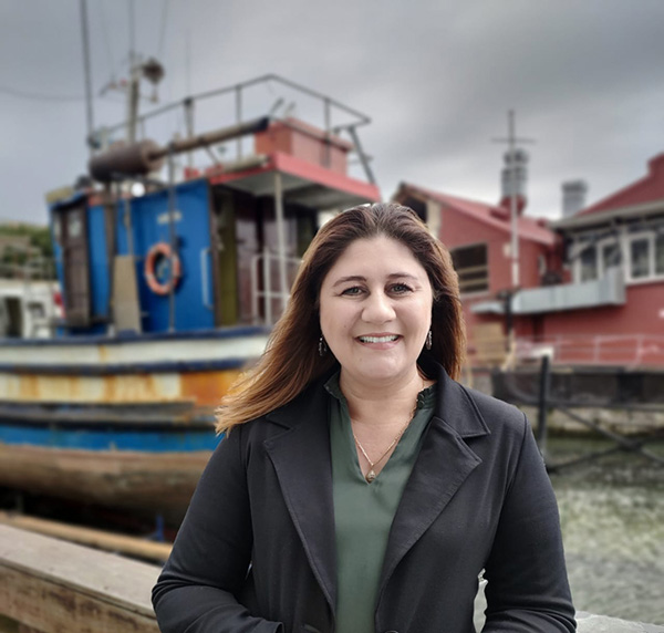 Marika van Rhyn, Hollard Marine’s Senior Business Development Manager posing in front a tugboat and some houses under a cloudy sky